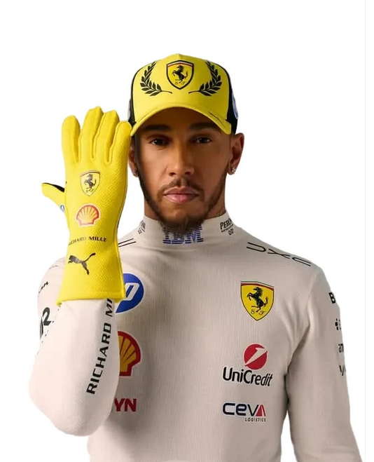 Lewis Hamilton in a white Ferrari racing suit and matching yellow cap, holding up a yellow racing glove with the Ferrari, Puma, and Shell logos, against a white background.